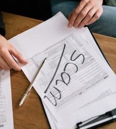 Close-up of hands on tax form with 'scam' written, highlighting tax fraud.