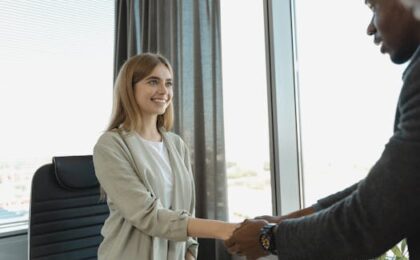 Woman smiling and shaking hands at a business office, signaling a successful job interview.